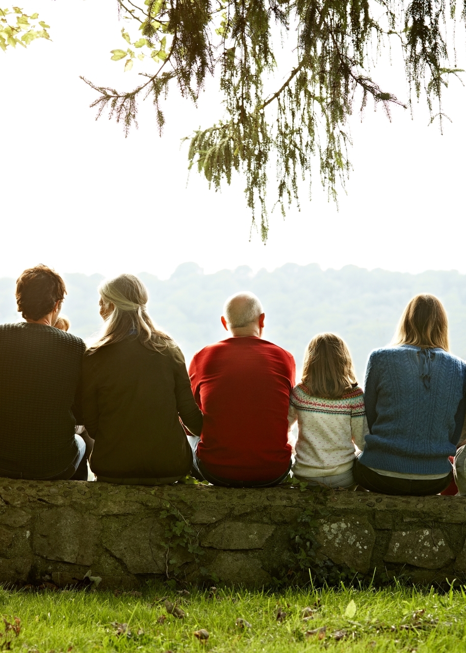  back view of a Multi-generation family sitting on retaining wall looking at a lake